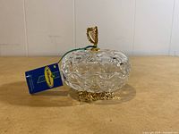Clear glass trinket dish with textured surface and gold harp handle on lid, tag attached.