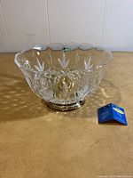 Clear 7-fluted crystal bowl showing cut lattice and etched leaf patterns with gold-finished base, viewed from a slight angle.