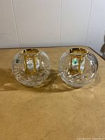 Two clear crystal rose bowl shaped tea light candle holders with 22CT gold finish on top rims and the candle holder inside, placed side by side on a wood surface.