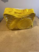 Yellow and clear plastic carrying bag holding plates and utensils for picnic set
