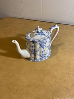 Porcelain teapot showing front angle, highlighting spout and blue floral pattern on white base.