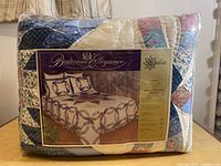 Photo of packaged quilt set showing Bedroom Elegance branding and design image of patchwork blue and cream quilt with matching pillows.