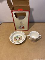 Opened original Royal Doulton Bunnykins box with bowl and baby cup placed in front on a table.