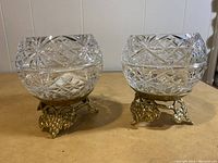 Two clear cut crystal votive candle holders with brass bases featuring grape and leaf designs, viewed from front