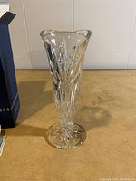 Crystal vase with flared top, decorative cut pattern, placed on a surface showing detail of the vase shape and design.