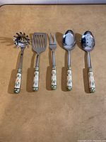 Five cooking utensils lined side by side on a table, showing the full utensils from handle to head.