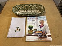 Photo showing the Temptations Old World bread bowl, white cloth napkins with embroidery, and the Temptations cookbook on a table.