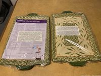 Two rectangular Temptations Old World green cookie sheets in original plastic packaging, showing front and back sides with decorative pattern and partial labels.