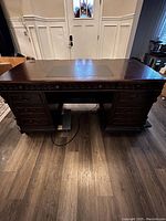 Front view of large traditional wooden desk in rich brown finish with multiple drawers and central leather writing pad.