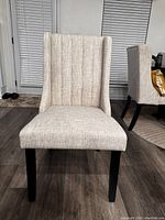 Front view of a beige upholstered Parsons style dining chair with tall back and soft fabric seat, sitting on wood floor.