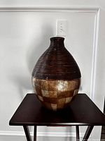 Photo of small decorative vase with checkerboard pattern and ribbed neck on dark table against white wall.
