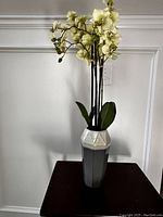 Full view of the small decorative vase holding a plastic orchid plant with cream flowers and green leaves.