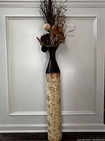 Tall decorative vase with natural branch arrangement placed against a white paneled wall.