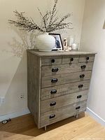 Wooden chest of drawers with 5 long drawers and 3 small drawers on top, placed against a wall with decorative items on top but not included in the lot.