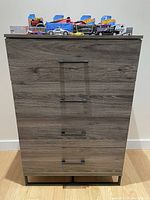Frontal view of the chest of drawers showing four drawers with black metal handles and a wood grain finish.