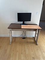 Desk with wood grain laminate top and silver metal frame against wall, cables below desk visible