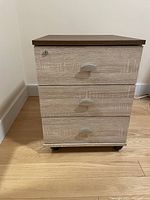 Front view of the 3-drawer filing cabinet with silver handles and locking mechanism on top drawer, showing light oak finish and darker top panel.