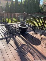 Photo of fire pit centered on deck with four black plastic chairs arranged around it.
