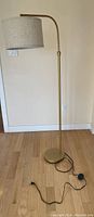 Full view of the gold floor lamp with fabric shade against a beige wall on wood flooring