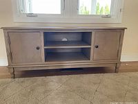 Front view of wooden cabinet with two doors closed and two central shelves with cord hole.