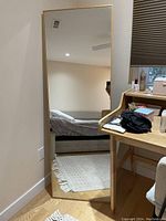 Full view of slim gold metal framed floor mirror leaning against wall next to desk