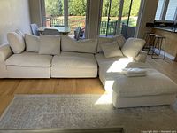 Full view of the beige four-seat sectional sofa positioned in a living room environment with a wooden floor and partially visible dining area.