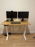 Full view of the Henglian standing desk with dual Dell monitors, Logitech keyboard and mouse on the desk surface, cables and power strips visible below