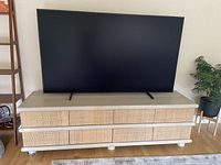 Front view of the TV cabinet with the TV on top, showing the wood grain laminate finish and eight wicker drawers.