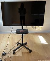 Full view of the Hisense TV mounted on a mobile stand with caster wheels, showing front of the screen and the stand with power cord on the floor.