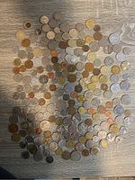 Photo showing a large assortment of various foreign coins spread on a grey wooden floor.