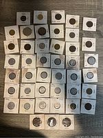 Photo showing 45 Italian coins arranged in 5 rows, each in white cardboard sleeves with handwritten dates ranging from 1867 to 1968. Sleeves show signs of wear and some discoloration.
