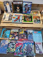 Overview photo showing a variety of comic books, art books, magazines including Batman, Robotech, Marvel Spider-Man, ThunderCats, and Comic Shop News.