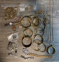 Photo displaying assortment of gold and silver costume jewelry including bangles, bracelets, necklaces, and smaller items in plastic bags.