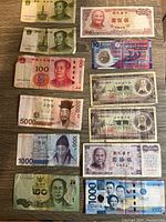 Overview of multiple foreign banknotes from Asia including Chinese yuan, Taiwanese, Korean, Japanese, Philippine, Thai, and Hong Kong notes arranged on a wooden surface.