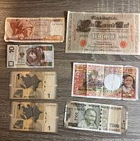 Top view of seven mixed foreign banknotes including German, Indian, French, and Polish currency on a wooden surface.
