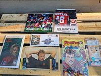 Top view of mixed Joe Montana memorabilia laid on wood surface including signed photo, printed images, and various collectible cards and items.