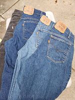 Top view of four folded pants showing variety of shades and textures: three denim jeans in dark, medium, and light blue, and one black corduroy pair, all with Levi's leather patches visible at waistbands.
