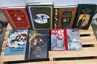 Nine books displayed on a wooden pallet surface, showing a variety of classic books and graphic novels.