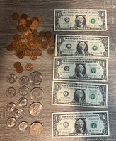 Photo showing five one dollar bills laid out with a pile of pennies and dimes, and several Eisenhower and Susan B Anthony dollar coins arranged below them.