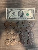 Photo of a $10 US Dollar bill with serial F03418371D and 16 Kennedy half dollar coins laid out on wooden surface