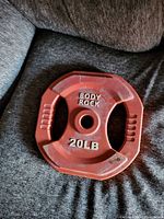 Red 20lbs Body Rock weight plate with grip handles, octagonal shape, showing wear