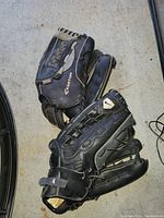 Two black baseball gloves on concrete surface. One is an Easton brand glove, the other Nike brand.