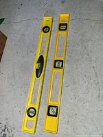 Two yellow spirit levels placed on concrete floor showing front side with multiple bubble vials and rubber grips.