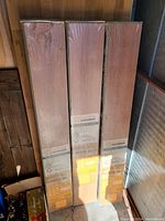 Three upright sealed boxes of Supra laminate flooring against wall, showing labels and packaging.