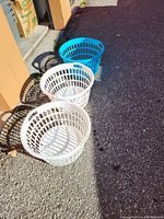 Three round plastic laundry baskets; two white and one blue, photographed outside on pavement in sunlight.