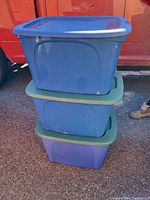 Stack of three large plastic storage totes, two with green lids and one with a blue lid on top, showing overall lot contents.