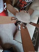 Ceiling fan with wooden blades and integrated frosted glass light fixture seen from the top and side angles.