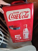 Front view of red Coca-Cola mini fridge with logo and bottle graphic. Chrome handle visible.