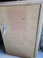 Rectangular cork board with a light wood frame, green push pin attached, and white paper scraps pinned on one side.