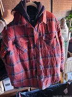Red and navy blue plaid Dakota coat on a hanger, showing the front with chest pockets and buttons.